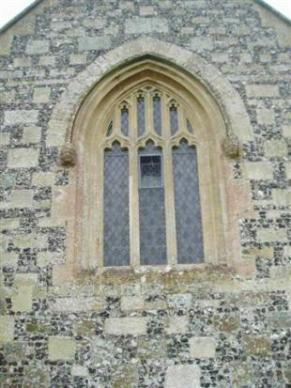 A stone wall featuring an arched window with intricate, stained glass designs. The window has multiple divisions and is framed with stonework. The wall is made of various sized stones, showcasing a mix of textures.