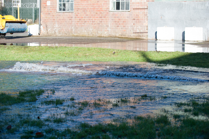 Flooded area with standing water and wet grass near a brick building, showcasing the impact of heavy rainfall or water accumulation.