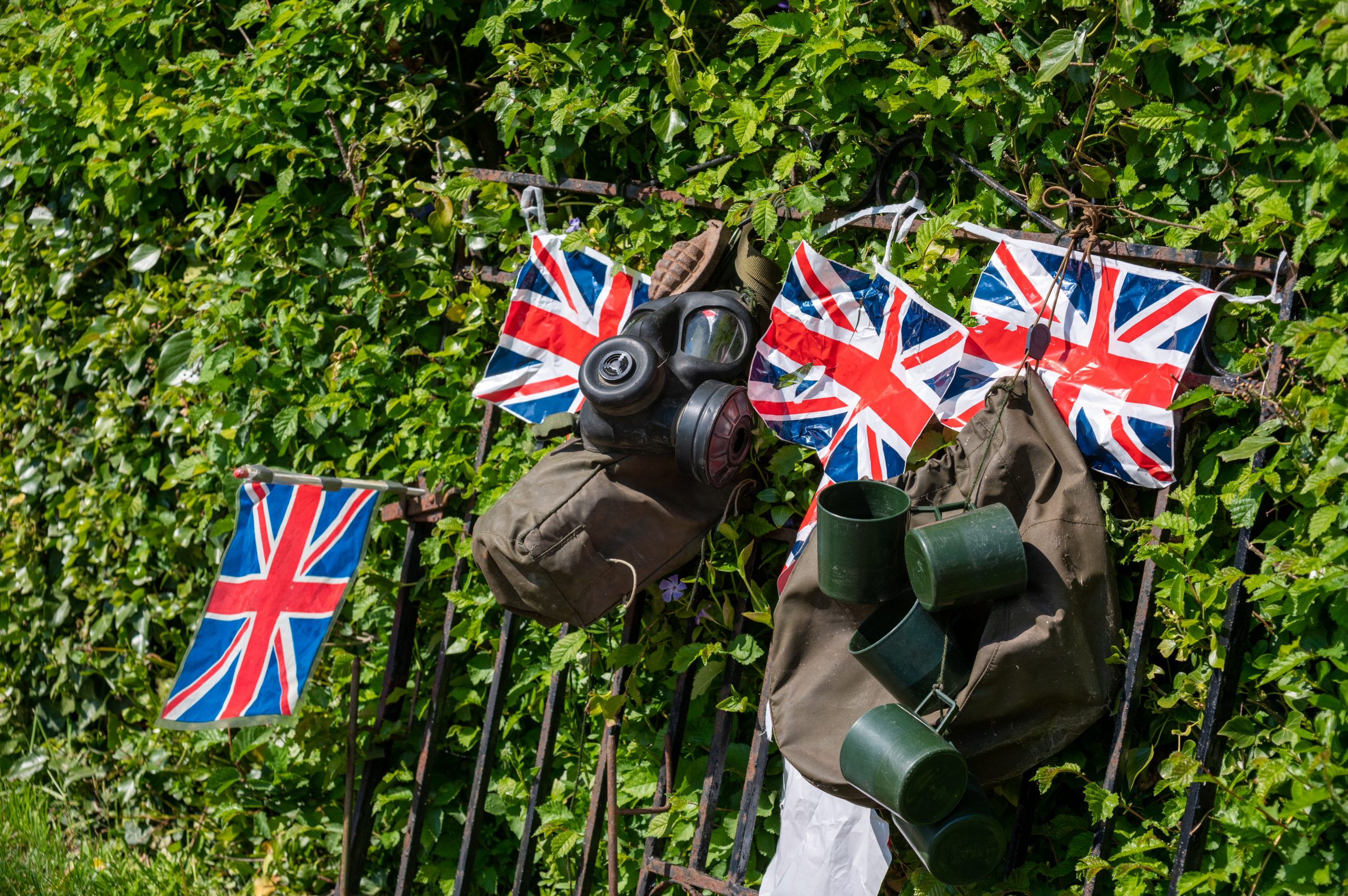 British flags and military gear hanging on a fence covered with greenery, symbolizing patriotism and historical significance.