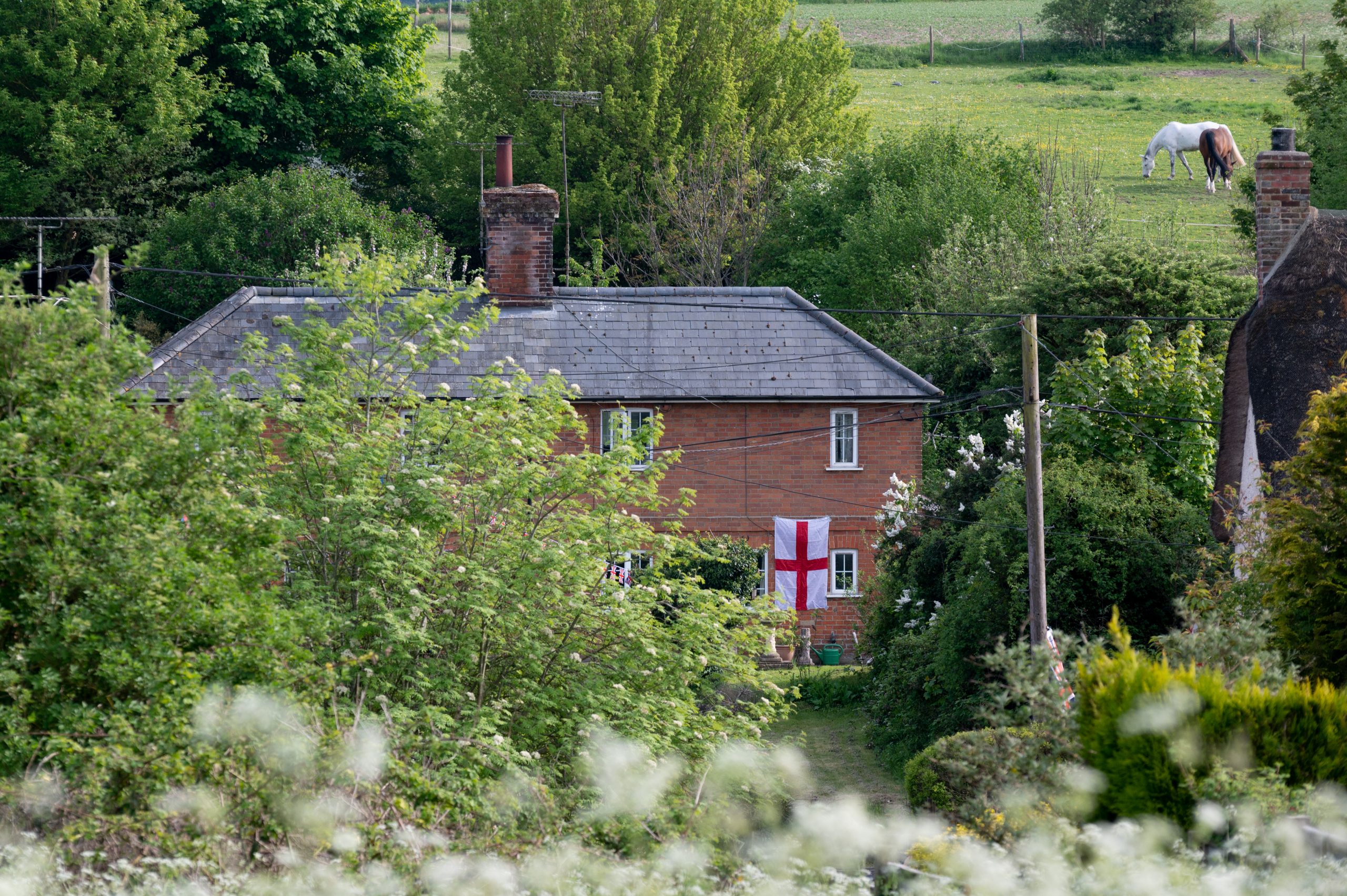Red brick house surrounded by lush greenery and trees, featuring a St. George's Cross flag, set in a rural English landscape.